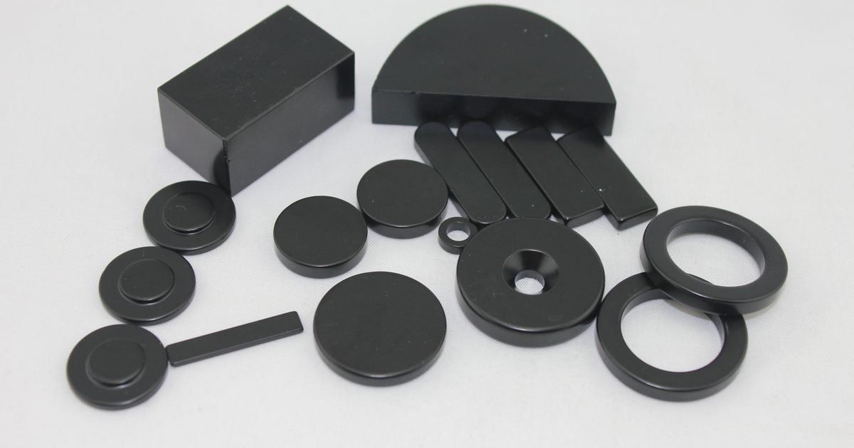 Black epoxy-coated neodymium magnets in block, disc, ring and arc shapes on a white background. Black epoxy-coated neodymium magnets in block, disc, ring and arc shapes on a white background.