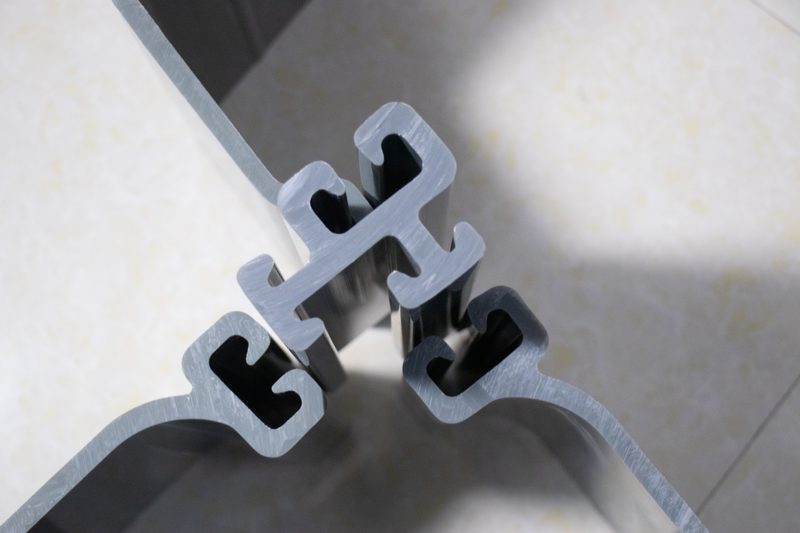 Gray PVC sheet pile profiles stored outdoors, showing the profile shape and stacked ends.