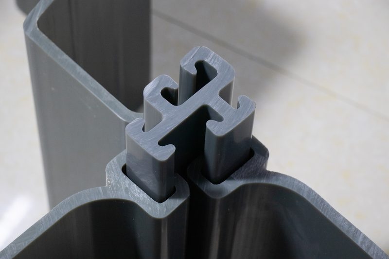 Gray PVC sheet pile profiles stored in outdoor racks, with profile ends and interlocks visible.