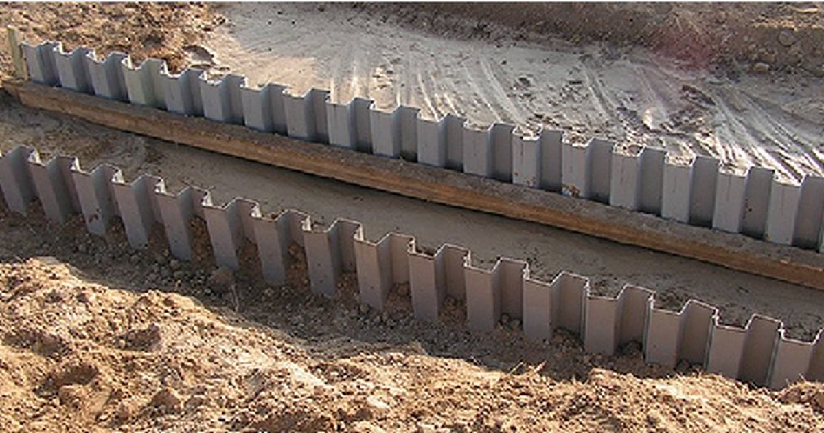 Gray PVC sheet pile wall being installed along an earthwork boundary with the interlocking profiles visible.
